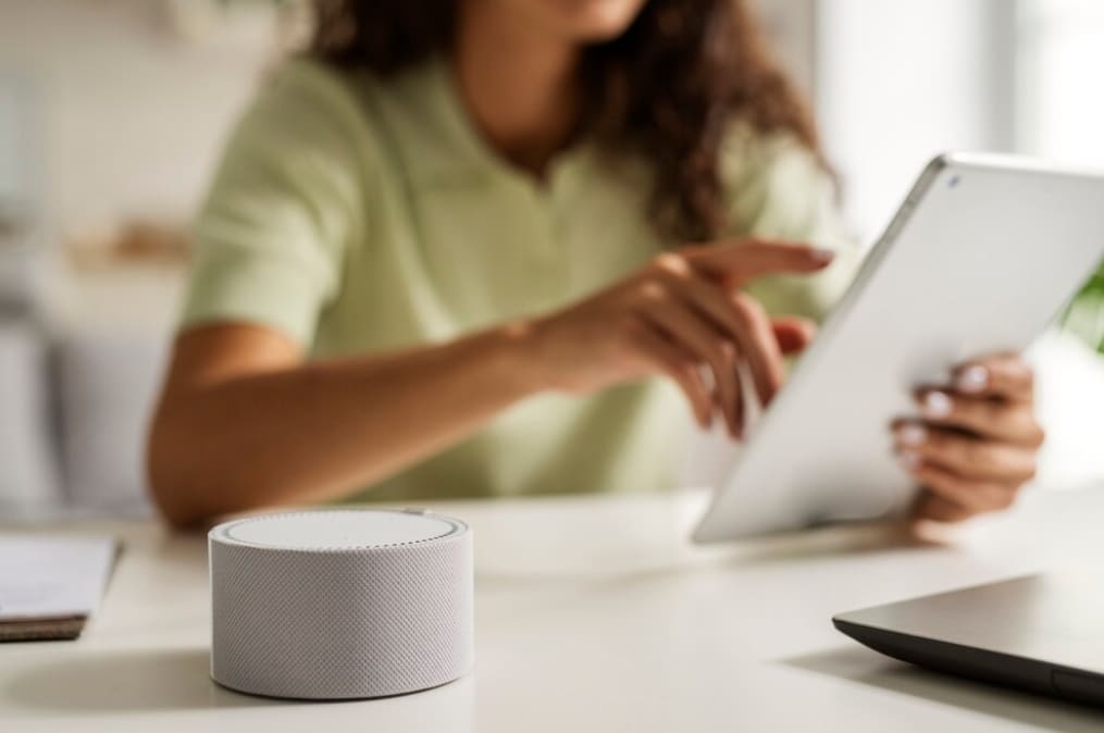 A smart speaker on a table as someone interacts with a tablet