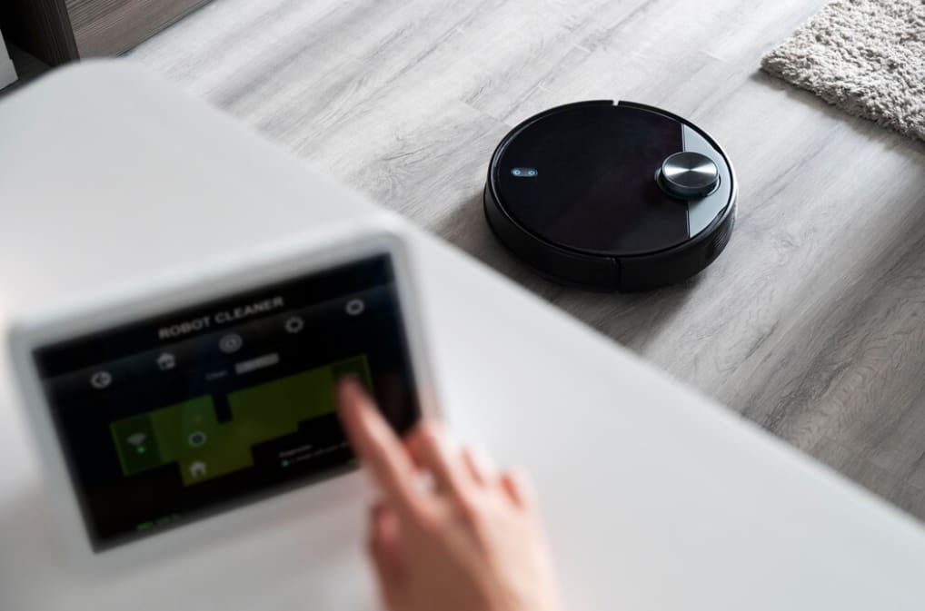 Person using a tablet to control a robotic vacuum cleaner on the floor